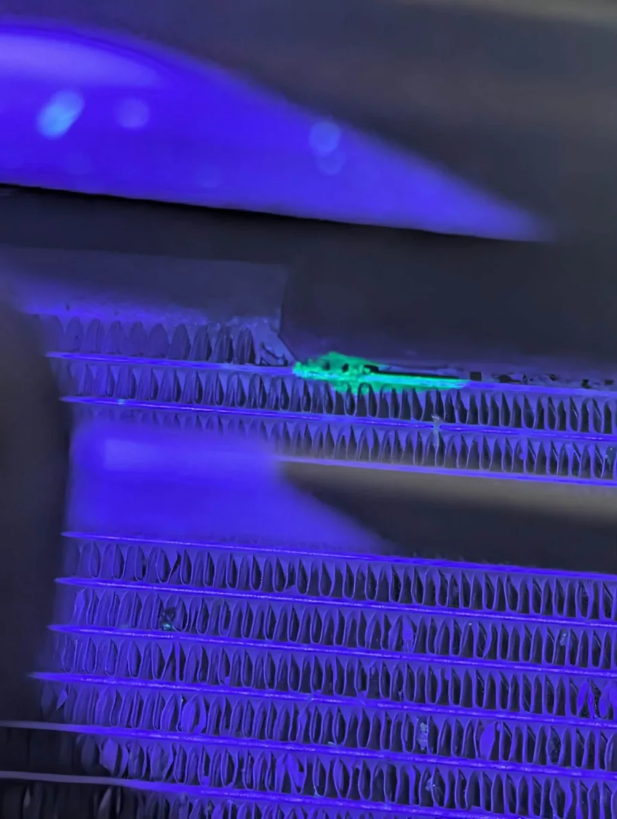 Fluorescent green leak-detection dye glowing under ultraviolet light on an air conditioning condenser at AutoNorth in North Bay