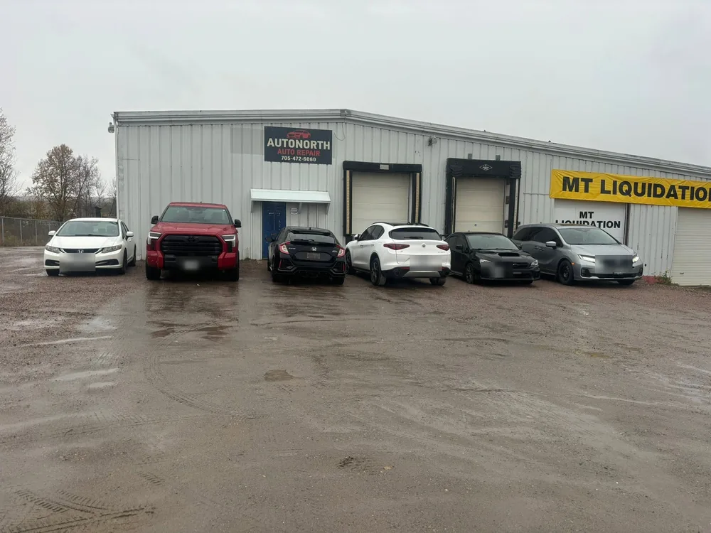 Grey steel-clad AutoNorth Auto Repair building in North Bay with two bay doors and customer cars parked on the gravel lot