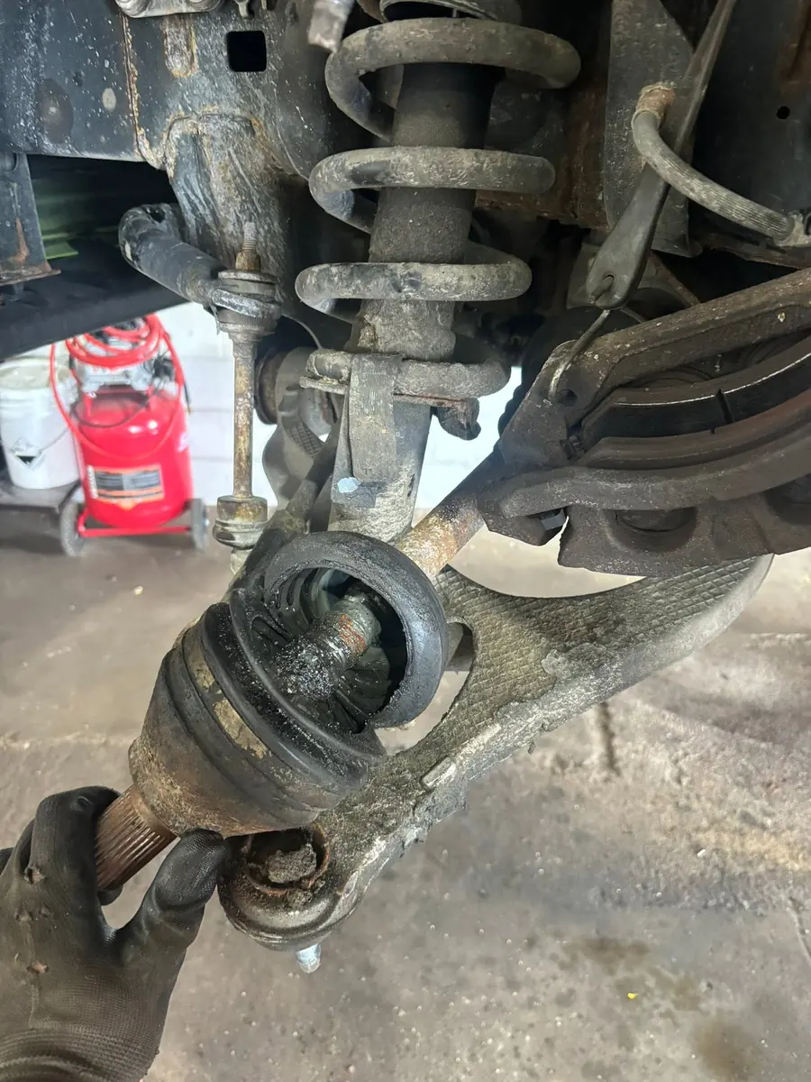 Underside view of a CV axle with the rubber boot split open and dark grease flung across the surrounding suspension components